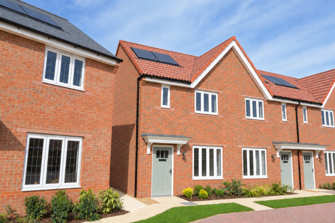 Modern red-brick houses with white-framed windows and solar panels stand behind a manicured green la