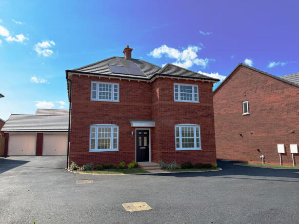 A red brick house with white-framed windows and solar panels on the roof sits on a paved driveway