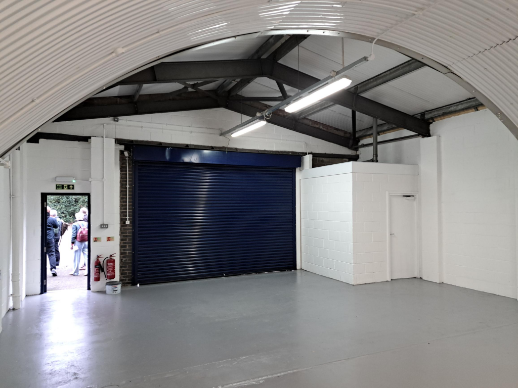 The front of an arch, with high level glazing, a closed electric roller shutter entrance big enough for vehicle access, and a pedestrian door.