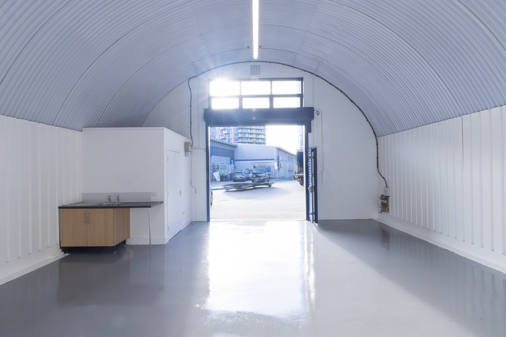 An empty arch with lining, facing the front electric roller shutter entrance, which is open. There is a WC cubicle at the front of the unit.