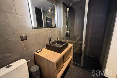 Modern bathroom with dark tiles features a glass-e