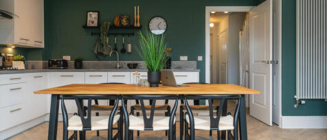 Modern kitchen with green accent wall, white cabinets, wooden dining table, and four chairs, with a