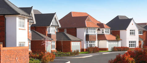 Modern houses with red and white exteriors, pitched roofs, and well-maintained gardens under clear b