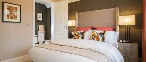 Modern bedroom featuring a large bed with colourful cushions, bedside lamps, and a view into the en-