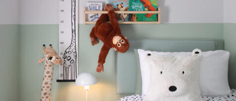 Children&#39;s bedroom with plush animal pillows, a hanging monkey toy, a giraffe lamp, children&#39;s books