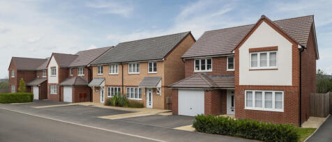Modern suburban houses with brick and white facades, pitched roofs, and driveways under a partly clo