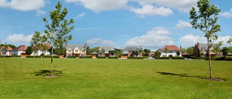 Modern residential houses with well-kept lawns and young trees under a blue sky with scattered cloud