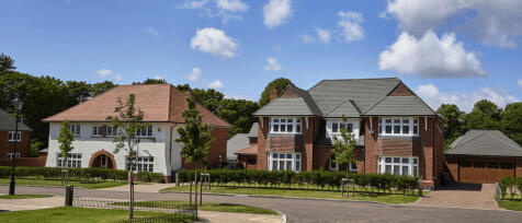 Two large modern houses, one white with a red-tiled roof and the other red brick with gray roofing,