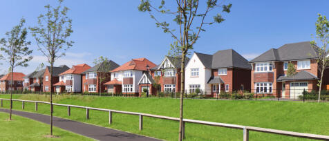 Modern suburban houses with brick and white exteriors, surrounded by young trees and a clear blue sk