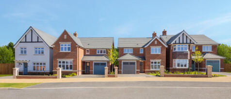 A row of modern detached houses with red brick exteriors, white and black timber detailing, and well