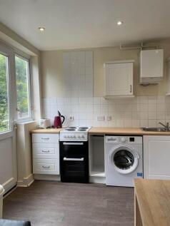 Bright fitted kitchen with white cabinets, elec...