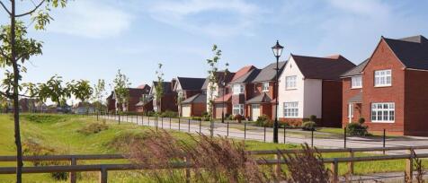 A row of modern detached houses with brick facades and pitched roofs along a quiet suburban street,