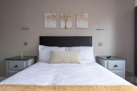 A neatly made double bed with white linens and ...