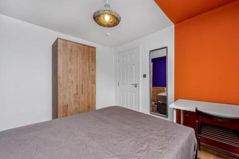 A well-lit bedroom featuring a bed with a soft,...