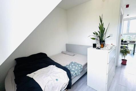 A well-lit bedroom featuring a simple bed with ...