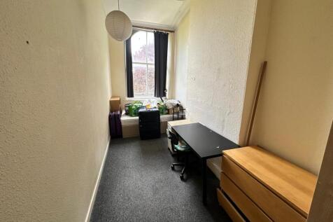 A cozy single bedroom with a desk and storage, ...