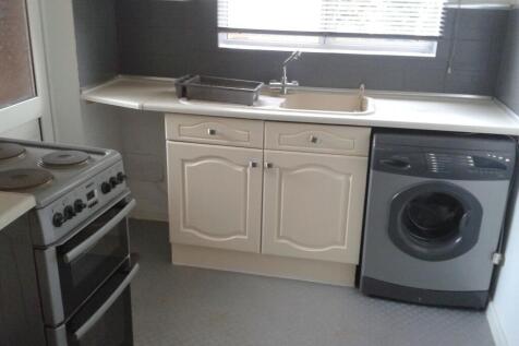 A compact kitchen featuring cream cabinetry, a ...