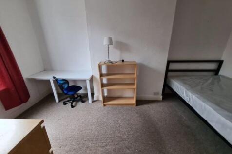 A tidy single bedroom featuring a bed, a desk w...