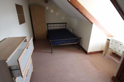 A cozy single bedroom featuring a slanted ceili...