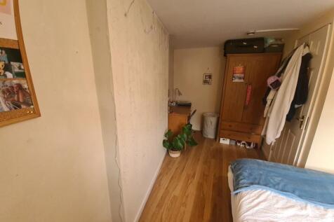 A cozy single bedroom featuring a wooden floor,...
