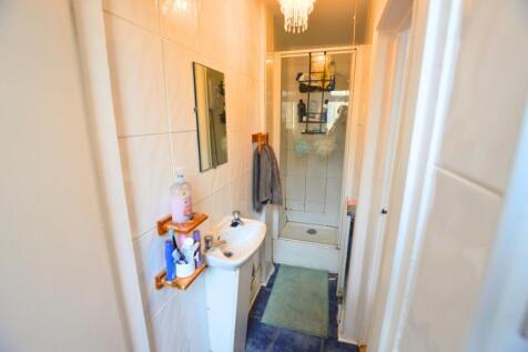 A narrow bathroom featuring a compact shower en...