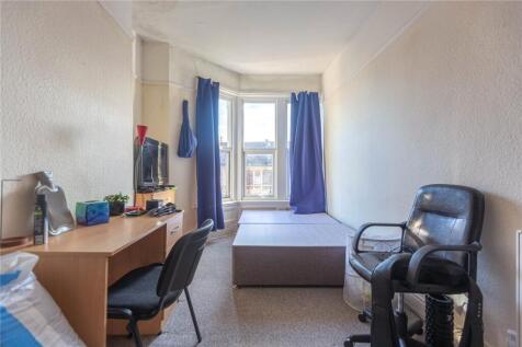A cozy single bedroom featuring a desk with cha...