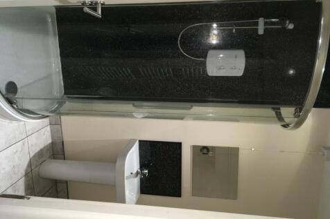 A modern bathroom suite featuring a curved glas...
