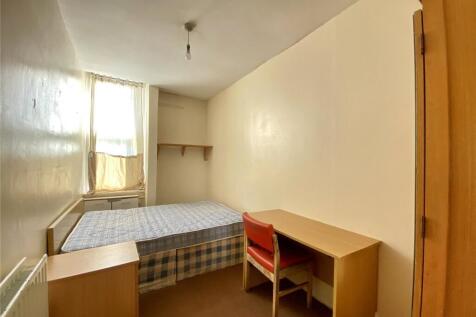 A cozy single bedroom with a neat bed, wooden d...