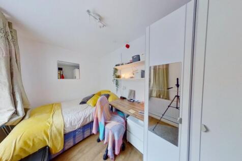 A bright single bedroom featuring a cozy bed wi...
