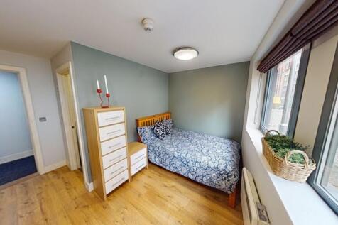 A cozy single bedroom featuring a wooden floor,...
