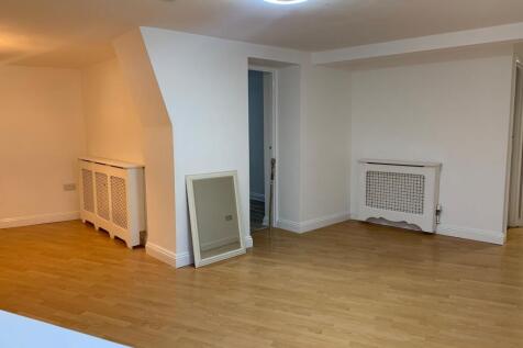 A spacious, clean living room with light wood f...