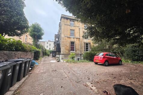 Stone-built period building set behind mature t...