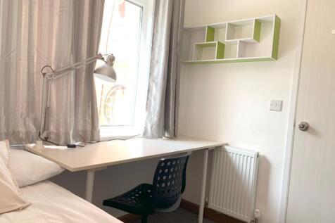 A cozy single bedroom with a neat study desk po...