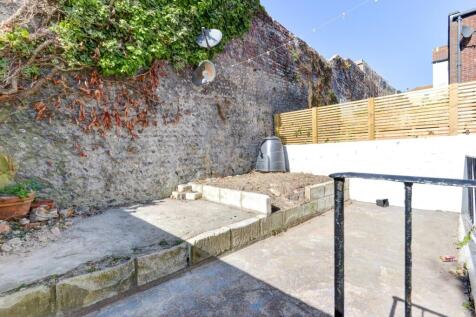 A bright, sunny garden with a spacious paved ar...