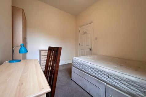 A cozy single bedroom featuring a wooden desk w...