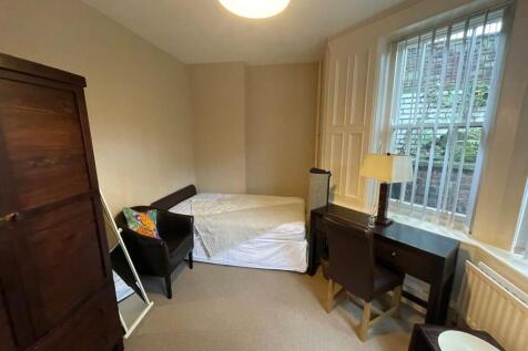 A cozy single bedroom featuring a bed, a wooden...