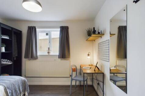 A bright and tidy bedroom featuring a bed, desk...