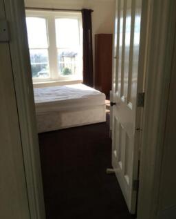 A double bedroom with a bed frame and large win...