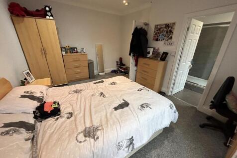 A well-lit bedroom featuring a large bed, wardr...