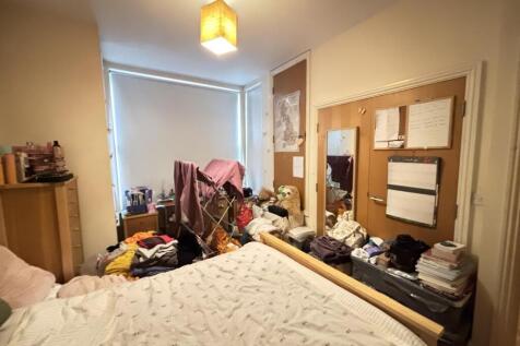 A cozy bedroom with a simple bed, cluttered sur...