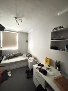 A modest bedroom featuring a single bed, a wind...