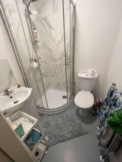 A modern compact bathroom featuring a corner sh...