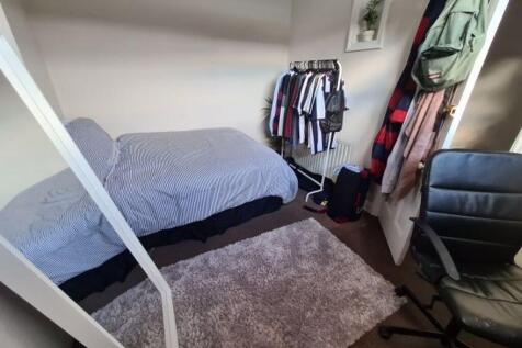 A cozy single bedroom featuring a bed, a window...