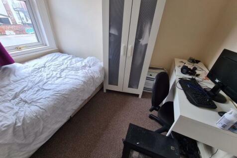 A neat and well-lit student bedroom featuring a...