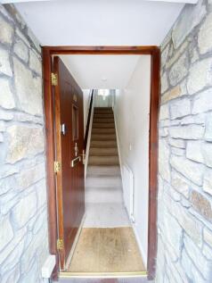 Open front door revealing a narrow carpeted hal...