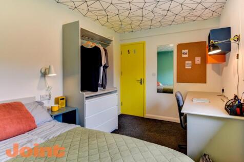 A cozy bedroom featuring a bed with a beige qui...