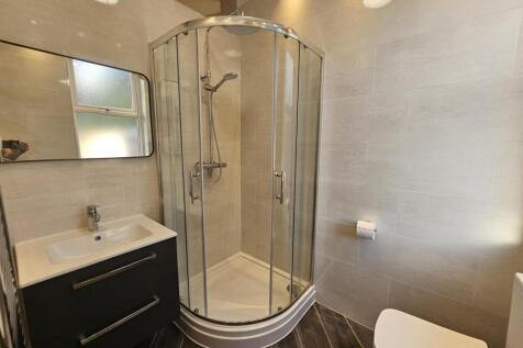 A modern bathroom suite featuring a curved glas...