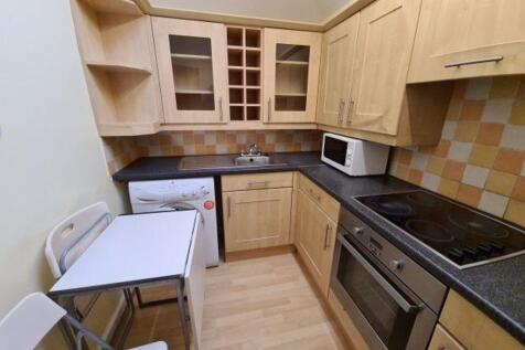 Compact fitted kitchen with light wood cabinets...
