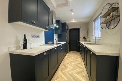 Modern galley kitchen with dark cabinetry, ligh...