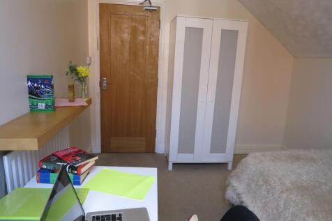 A cozy student bedroom featuring a wooden door,...